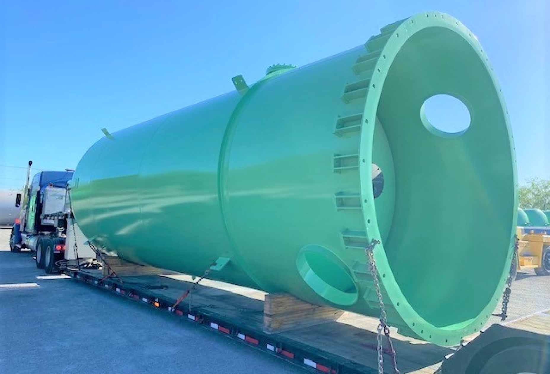 A large, green cylindrical load strapped to a truck low bed.