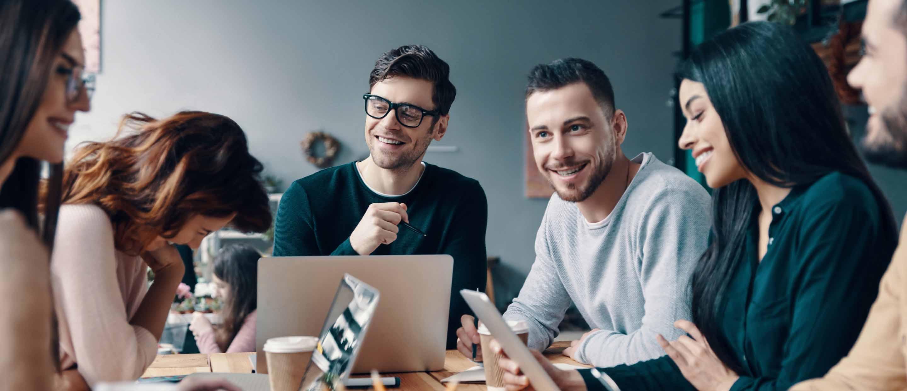 ZMac's team of transportation logistics experts sit and talk at a table with their laptops open.