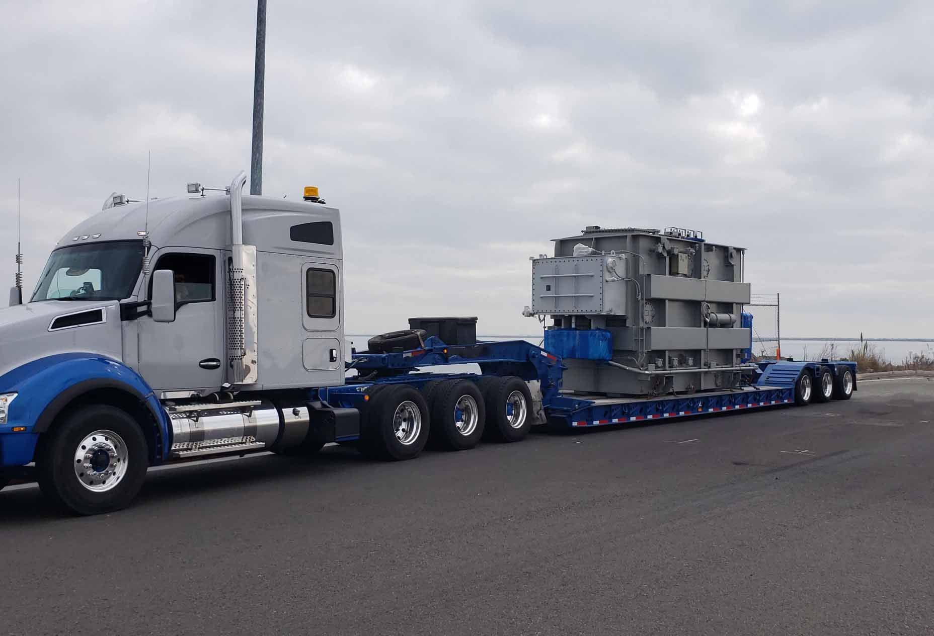 A truck carrying a load on a low bed drives toward a port.